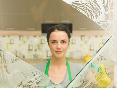 young beautiful housewife washing window at home